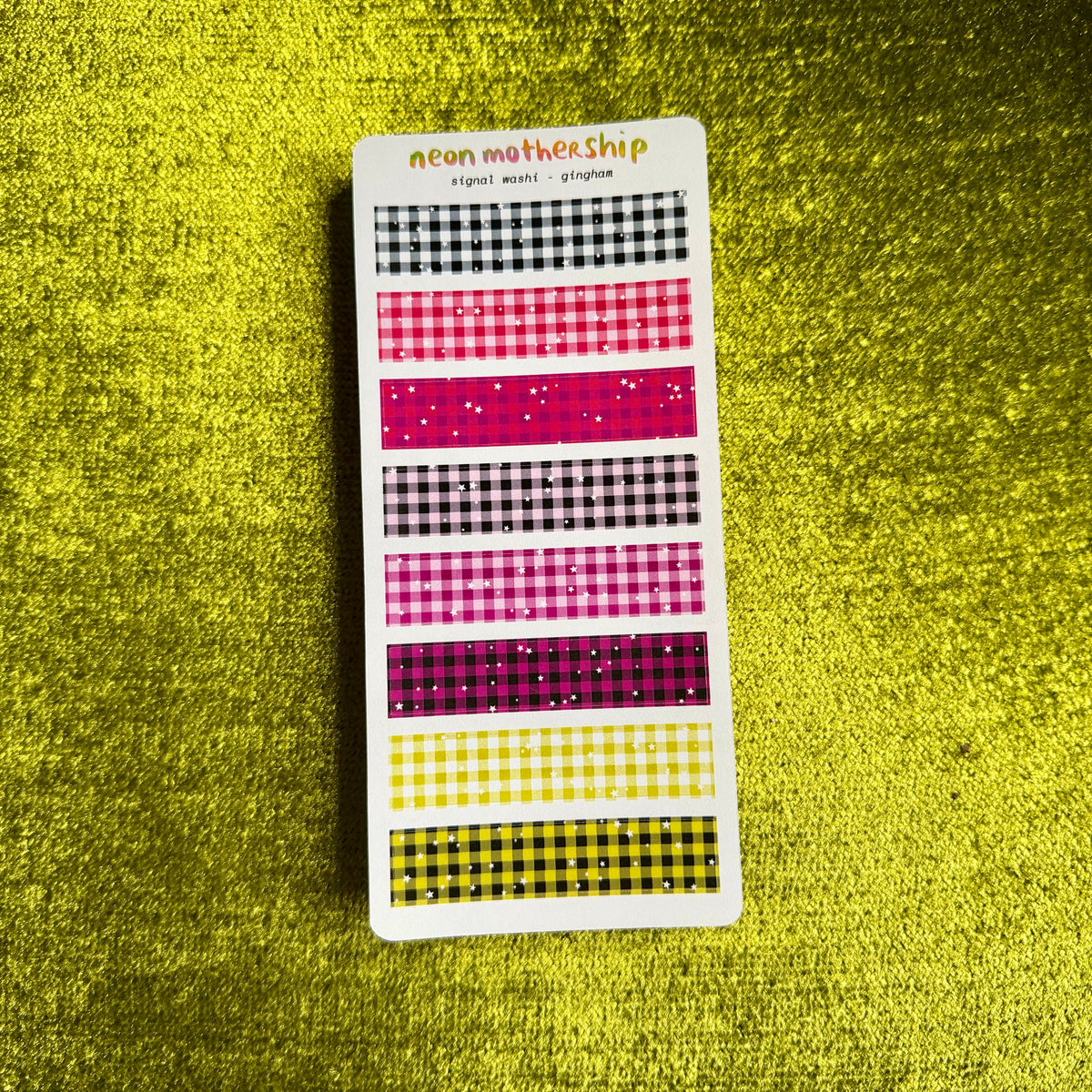 A vertical sticker sheet displaying multiple washi tape patterns in neon shades of pink, purple, yellow, and black, set against a textured yellow background.