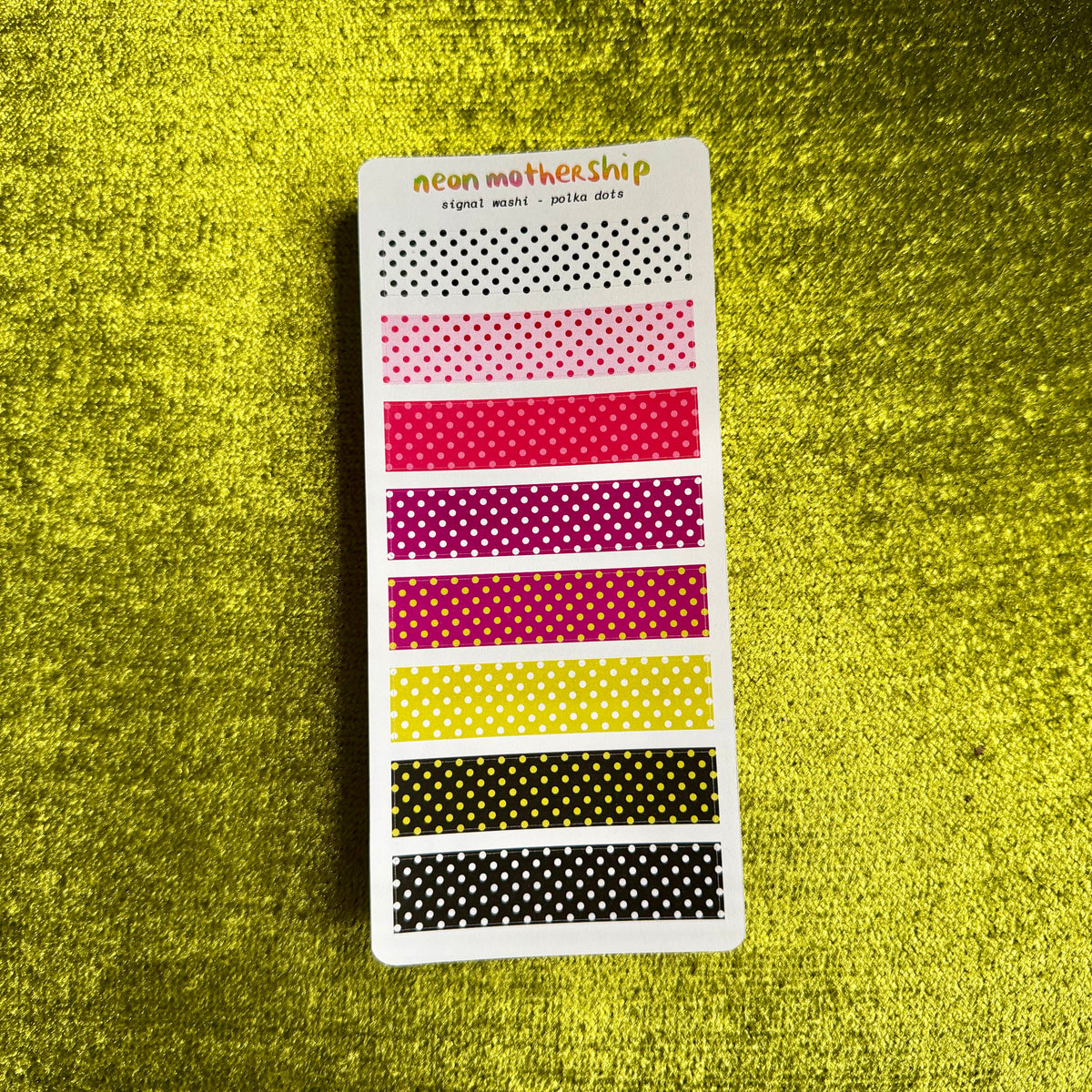 A vertical sticker sheet from neon mother ship featuring multiple horizontal rows of polka dot washi tapes in black, pink, red, magenta, yellow, and black, displayed on a textured yellow background.