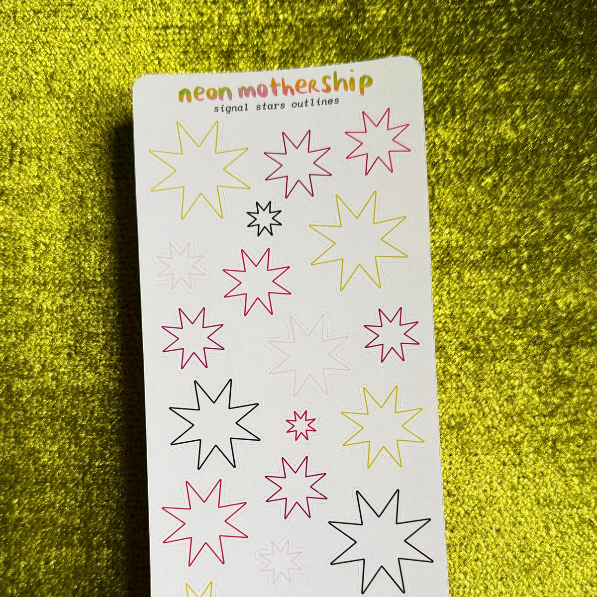 A sticker sheet from the brand 'neon mothership' featuring various neon-colored star and sparkle outlines on a white backing card, set against a textured yellow background.