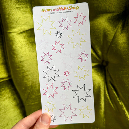 A hand holds a white sticker sheet featuring colorful neon star outlines, set against a bright yellow-green velvet fabric background. The sheet is titled 'neon mothership signal star outlines'.