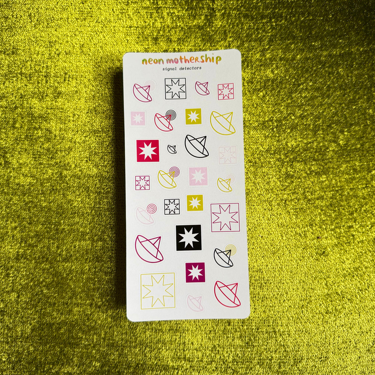 A rectangular sticker sheet from neon mothership called 'Detectors' featuring various colorful geometric and abstract shapes, placed on a textured green background.