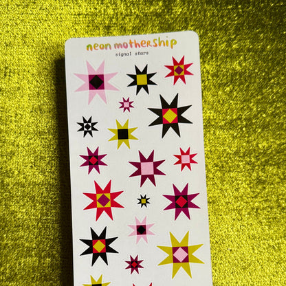 A rectangular sticker sheet titled 'neon mother ship' featuring various colorful starburst and geometric designs in pink, red, yellow, black, and white, displayed on a textured gold background.
