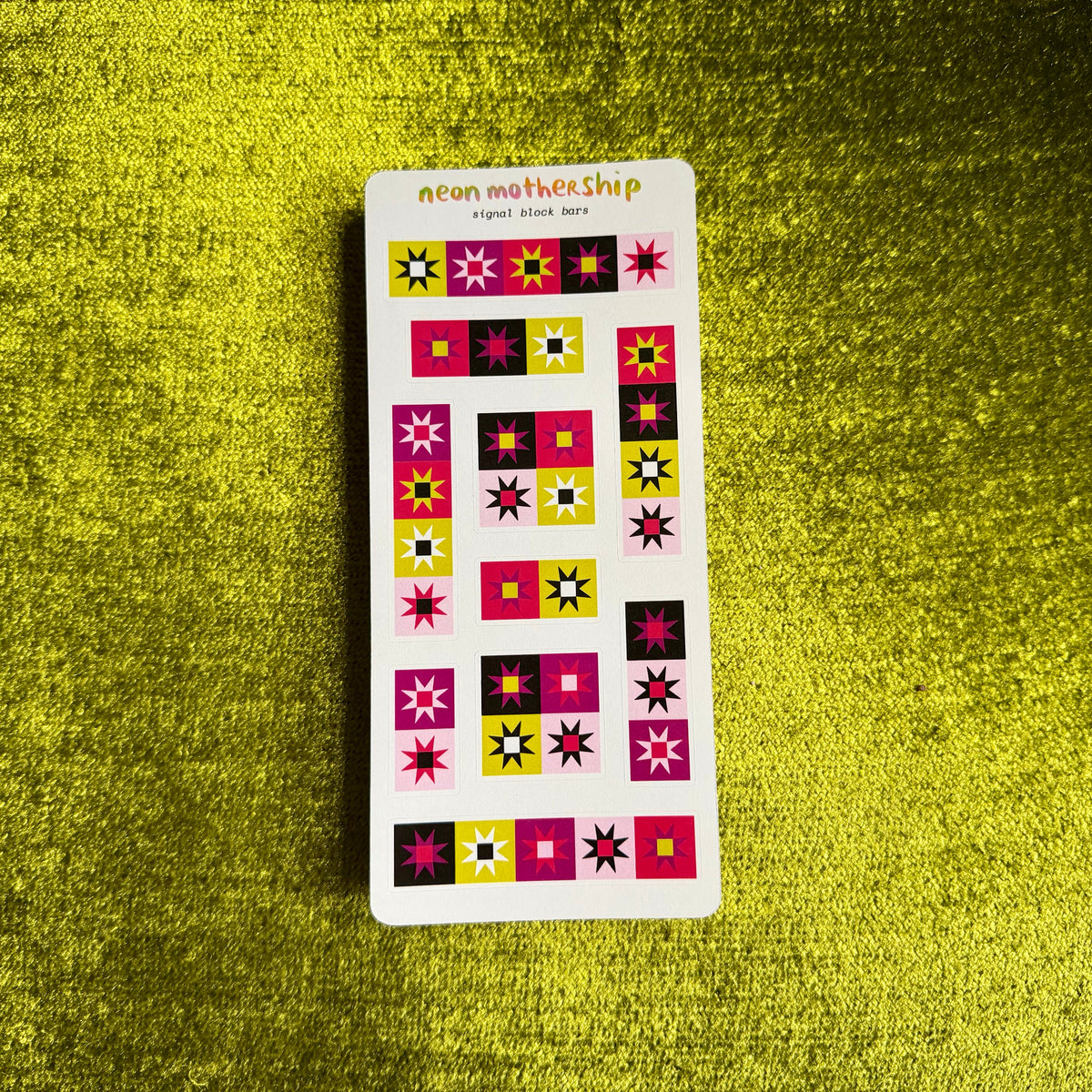 A sticker sheet from the brand 'neon mothership' featuring retro geometric flower and star stickers in pink, yellow, black, and white, displayed on a textured green background.