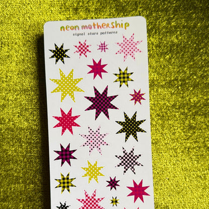 A sheet of neon mothership star patterns on a white backing card, displayed on a textured yellow-green background. The stars feature various neon colors including pink, purple, yellow, and green.