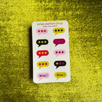 A sticker sheet titled 'neon mothership' featuring colorful speech bubble stickers with star patterns and text like 'wow!', placed on a textured green background.