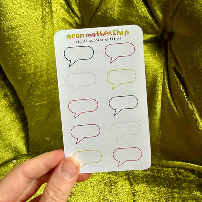 A hand holds a white sticker sheet featuring colorful outline speech bubbles, set against a shiny metallic olive green background.