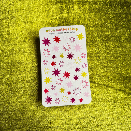 A rectangular sticker sheet from the brand neon mothership, featuring colorful star-shaped stickers in pink, yellow, and purple on a white background, placed on a textured yellow surface.