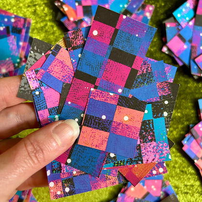 Colorful checkered sticker scraps held by a hand on a green textured surface