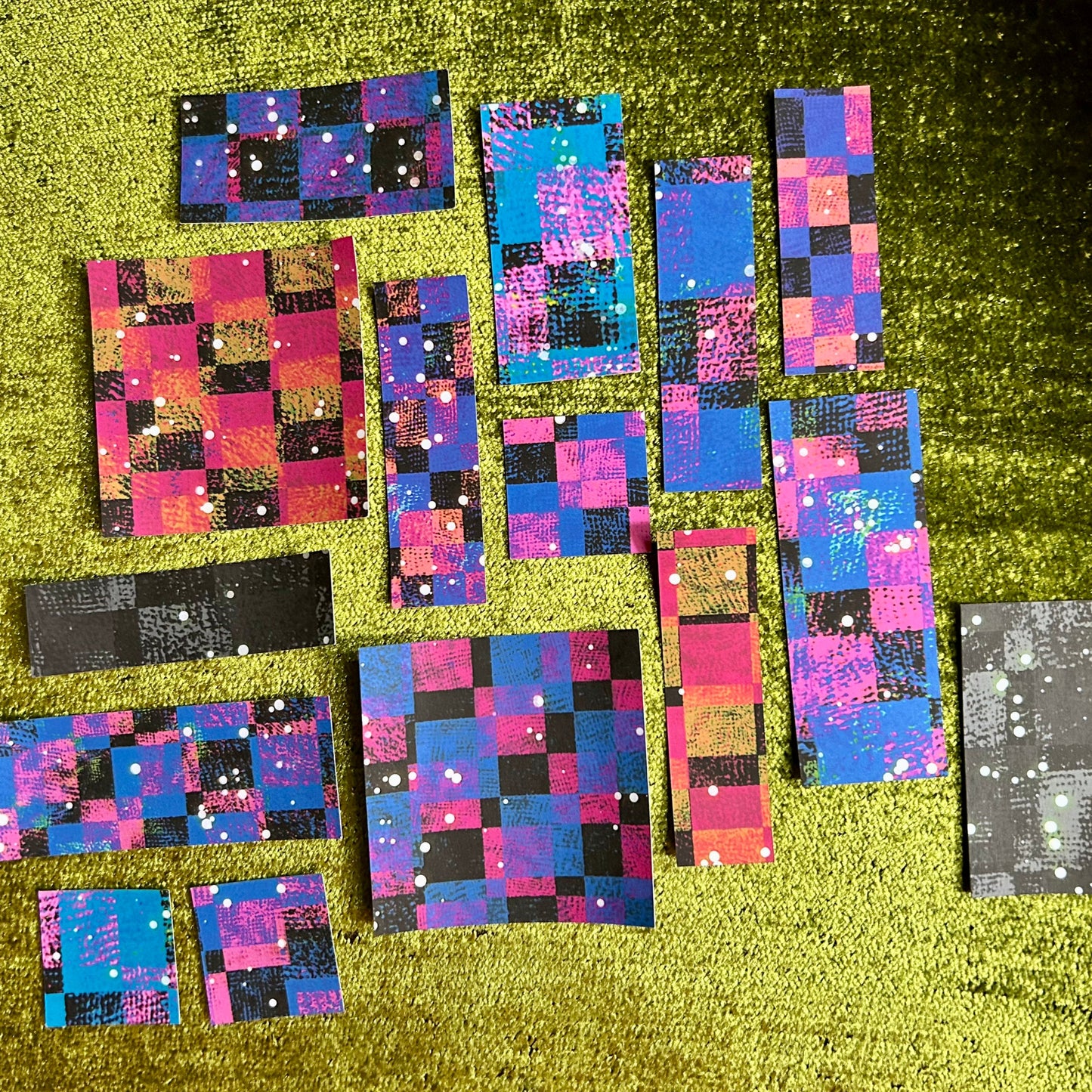 Collection of colorful checkered sticker scraps on a green textured surface