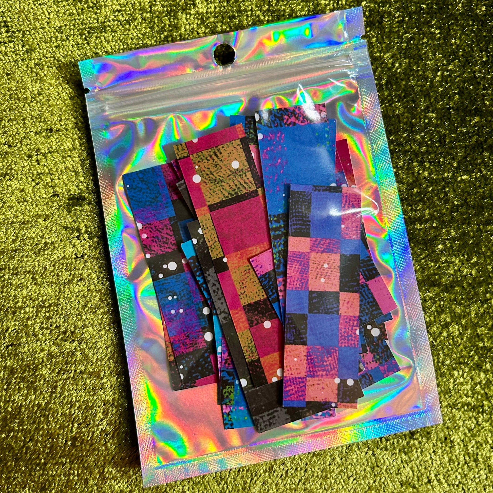 Holographic bag with colorful checkered sticker scraps on a green glittery background