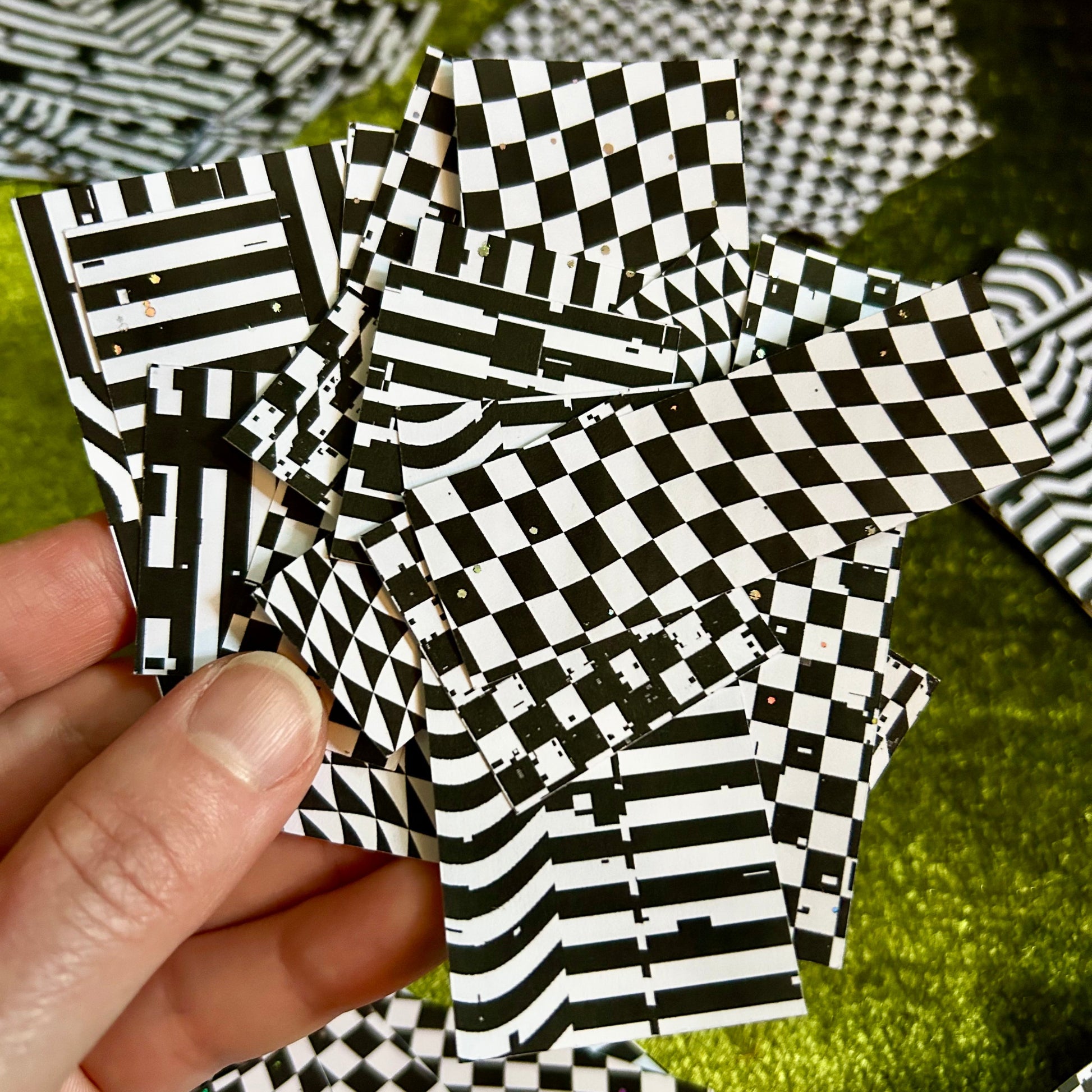 Black and white checkered paper strips held by a hand on a green surface