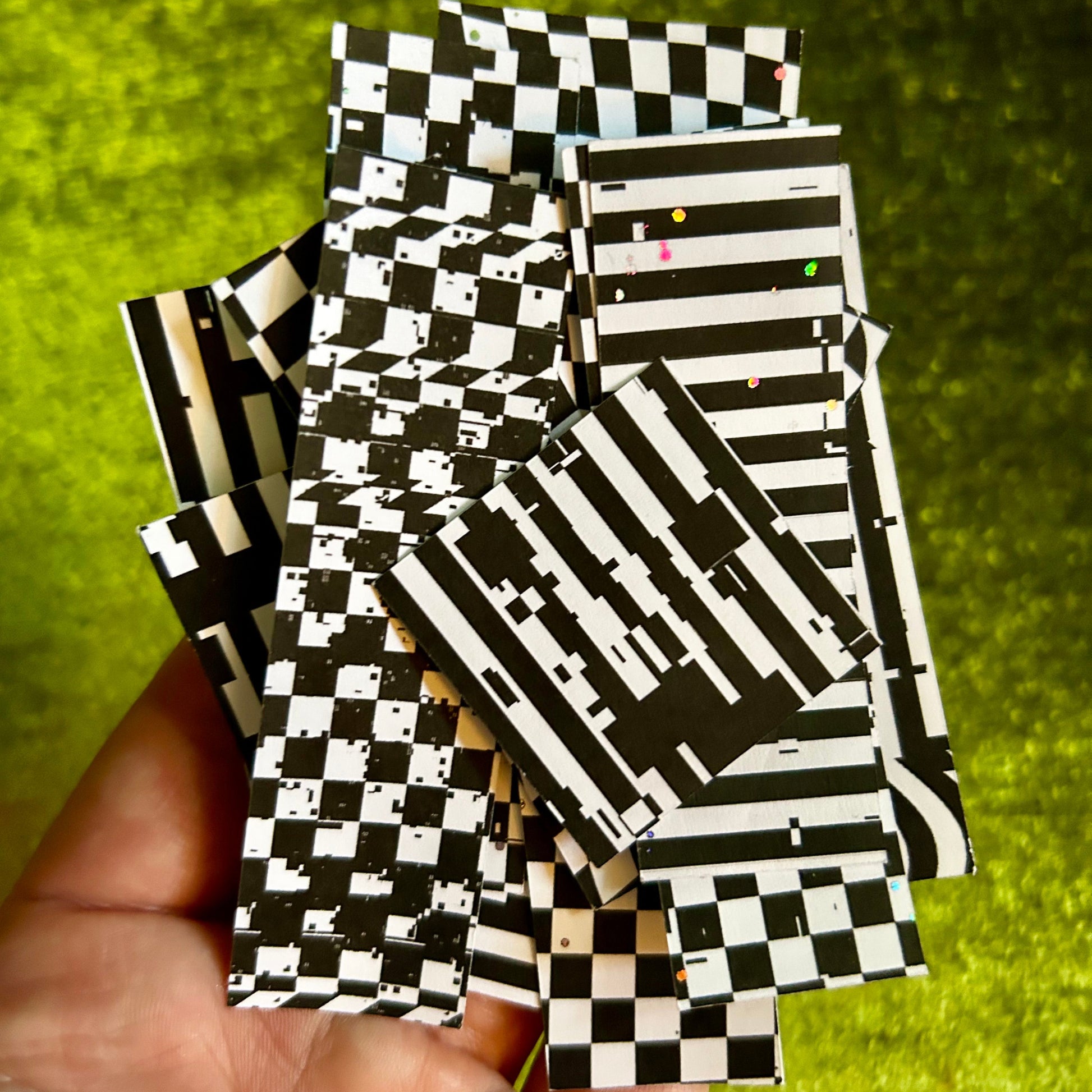 Black and white checkered paper sticker scraps held in a hand with a green background