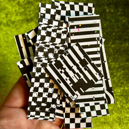 Black and white checkered paper sticker scraps held in a hand with a green background