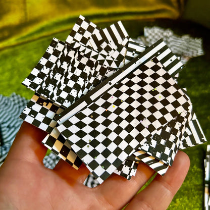 Hand holding black and white checkered paper against a green fabric background