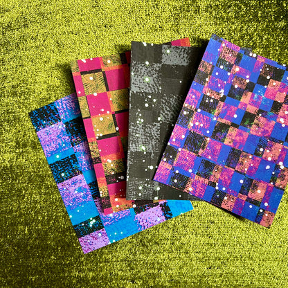 Four colorful checkered papers with glittery patterns on a green textured surface