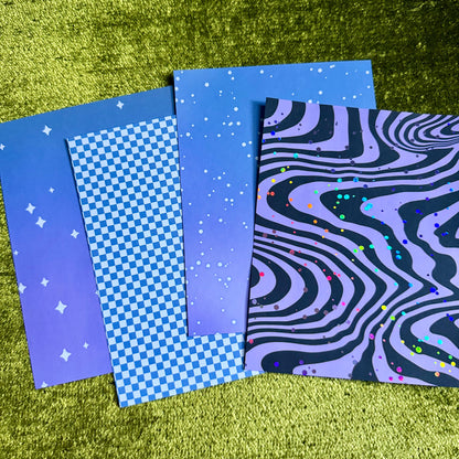 Four rectangular patterned sheets or cards arranged overlapping on a textured olive-green surface. The designs include a blue-to-purple gradient with white stars, a blue-and-white checkerboard pattern, a blue-to-purple gradient with white stars, and a black-and-purple wavy psychedelic pattern with small multicolored dots.