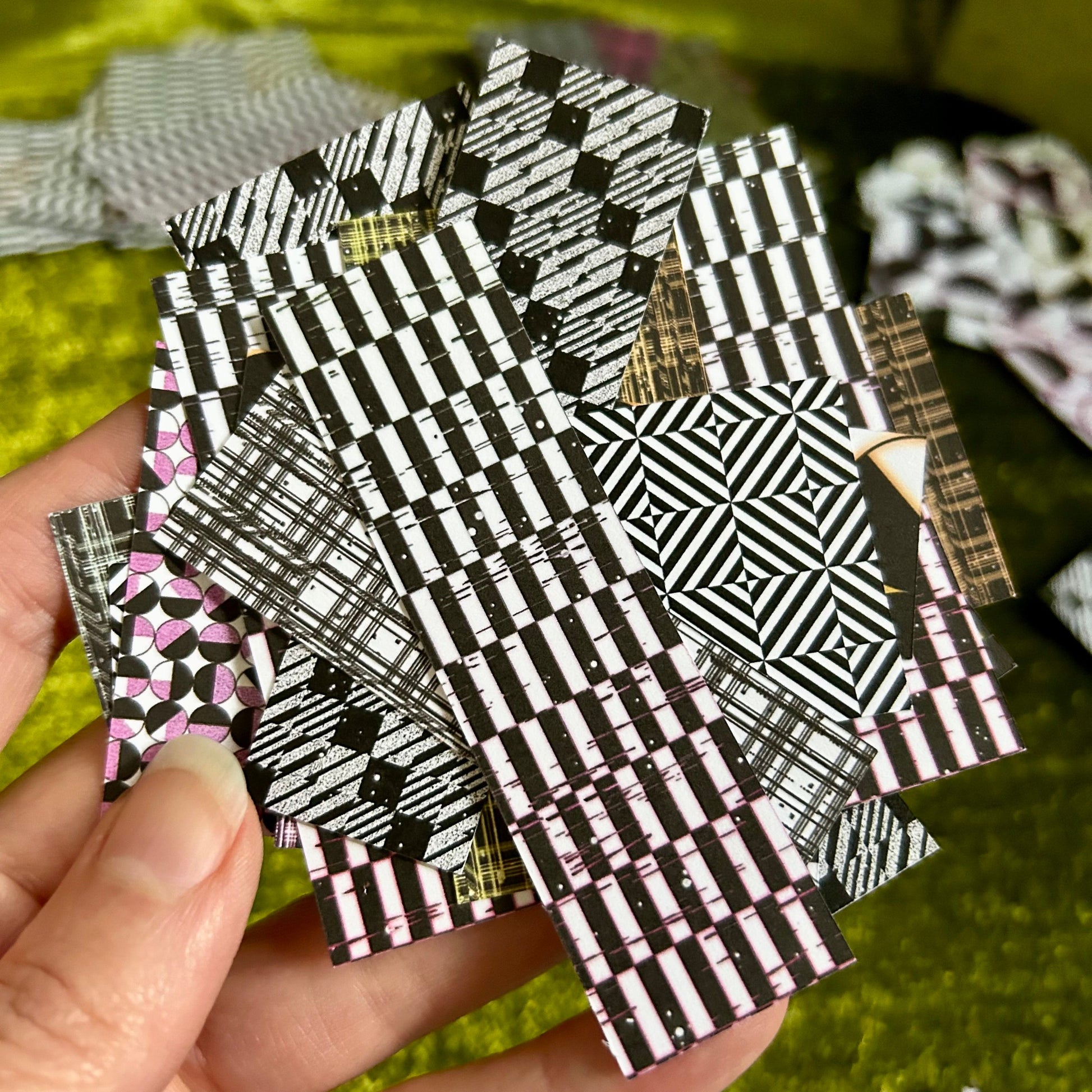 Hand holding a stack of black and white patterned sticker scraps with a blurred green background