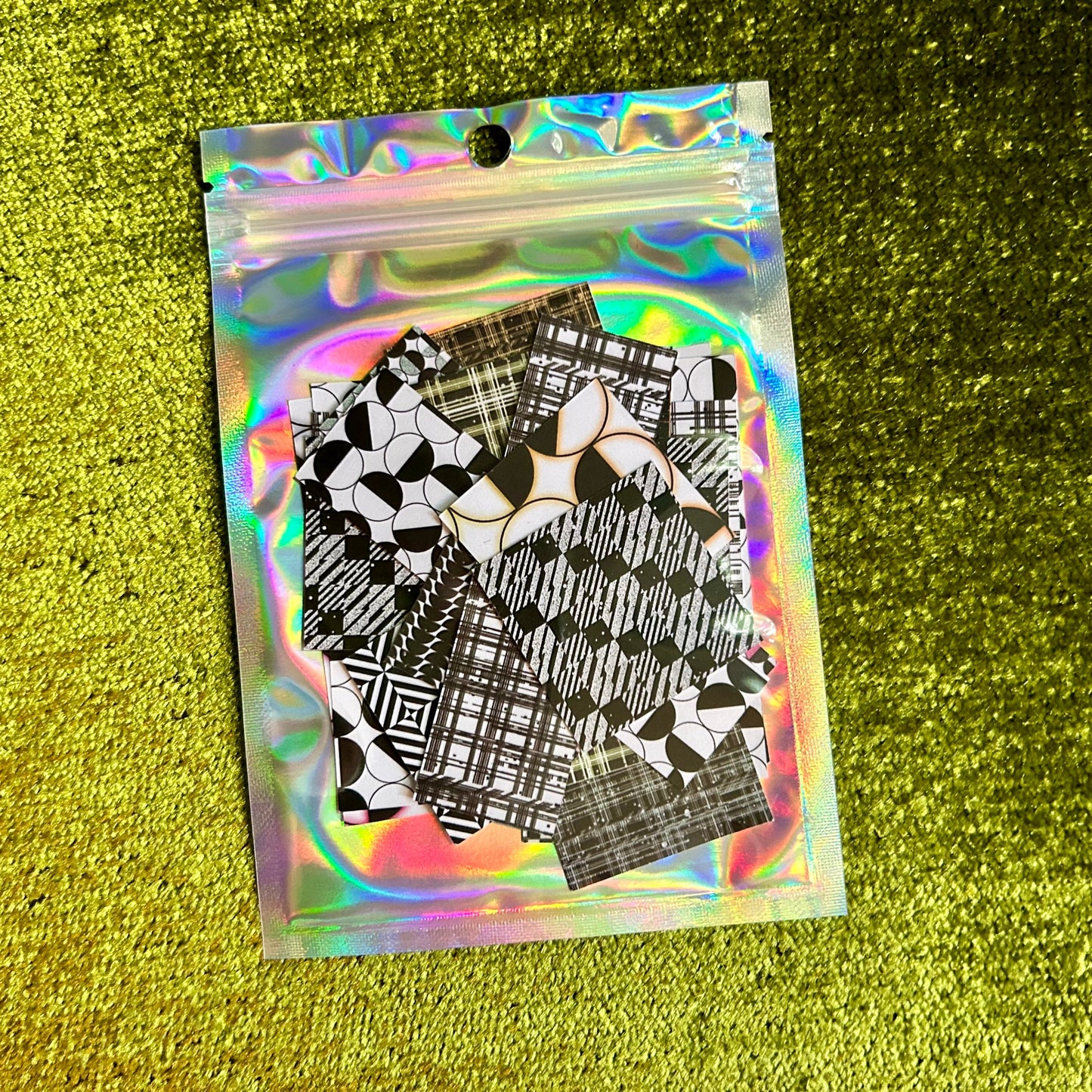 Holographic packaging with black and white patterned sticker sheets on a green textured background