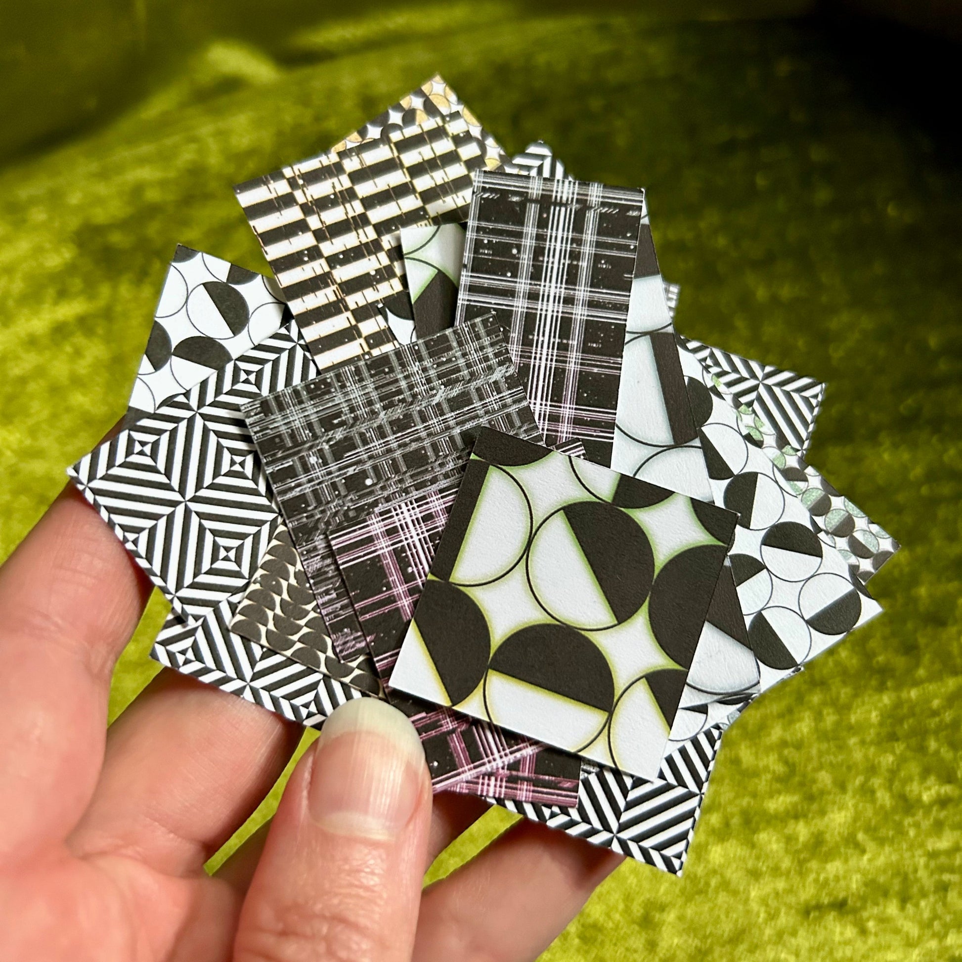 Hand holding a collection of black and white patterned sticker scraps against a green fabric background
