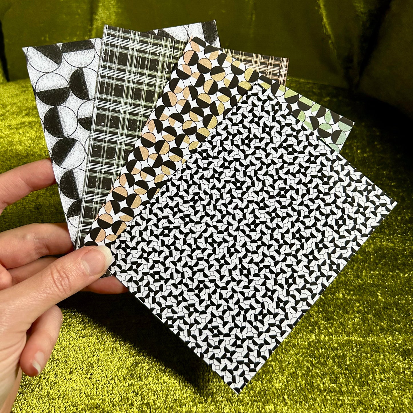 Four sticker papers with different patterns held by a hand against a green background