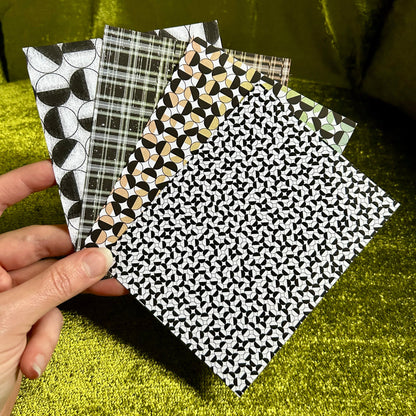 Four sticker papers with different patterns held by a hand against a green background