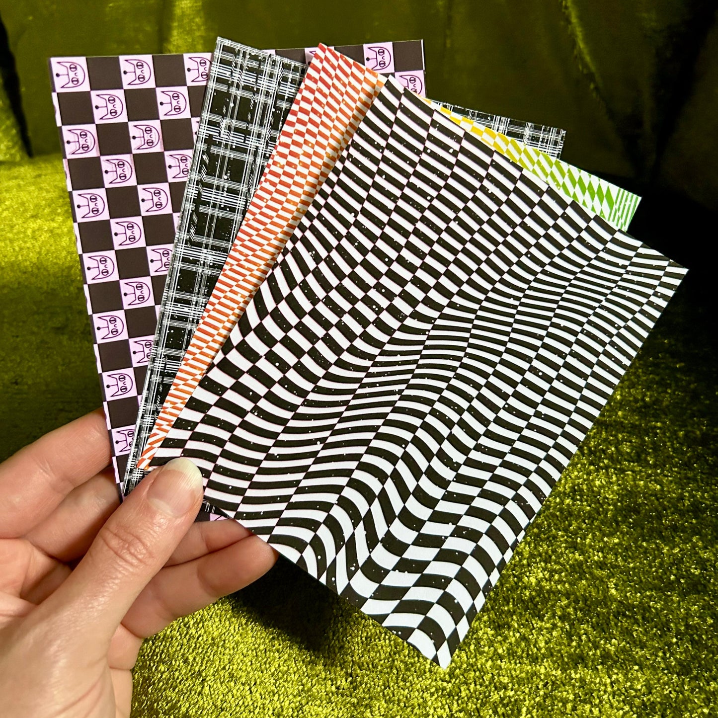 Hand holding four patterned sticker paper sheets against a green fabric background