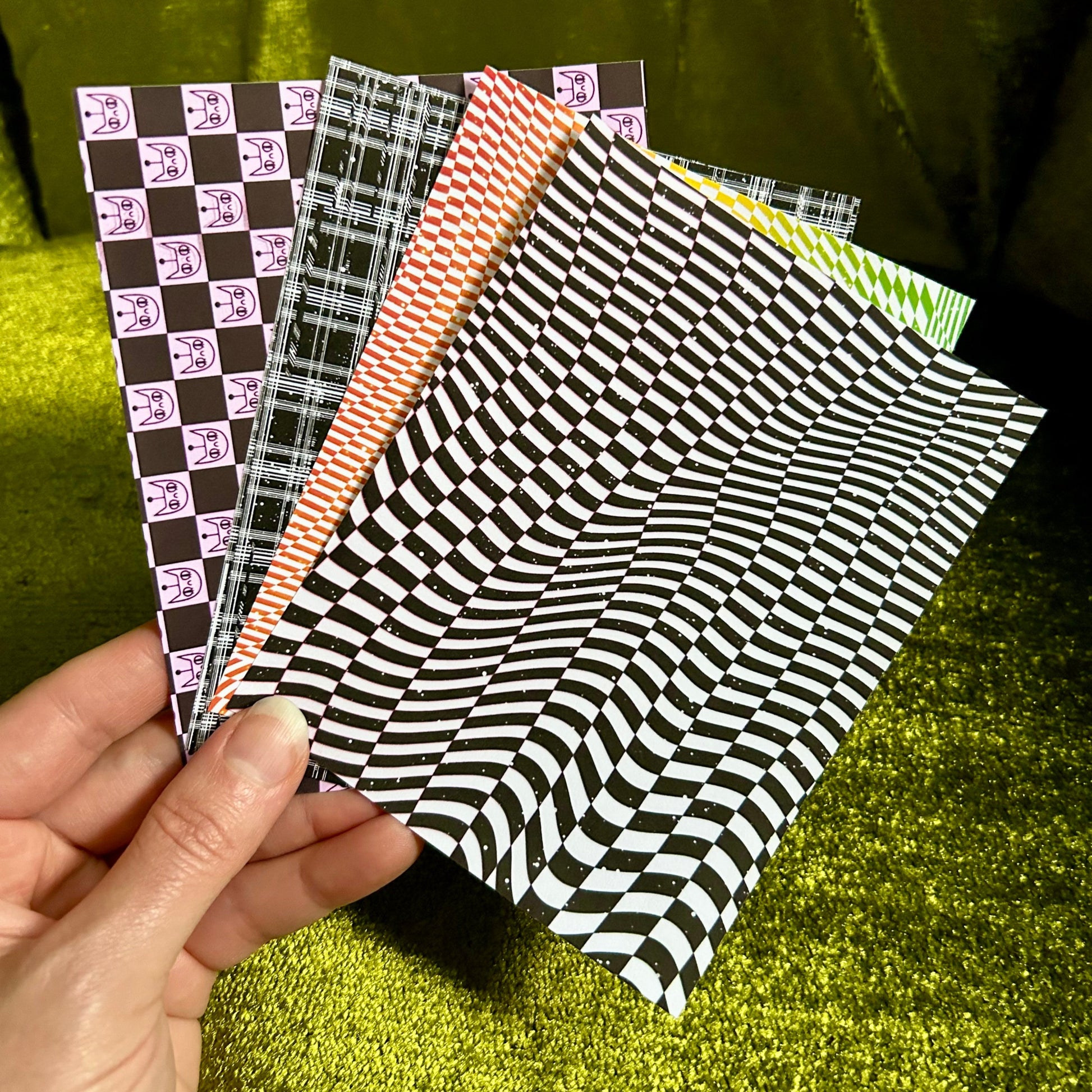 Hand holding four patterned sticker paper sheets against a green fabric background