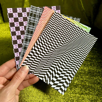 Hand holding four patterned sticker paper sheets against a green fabric background