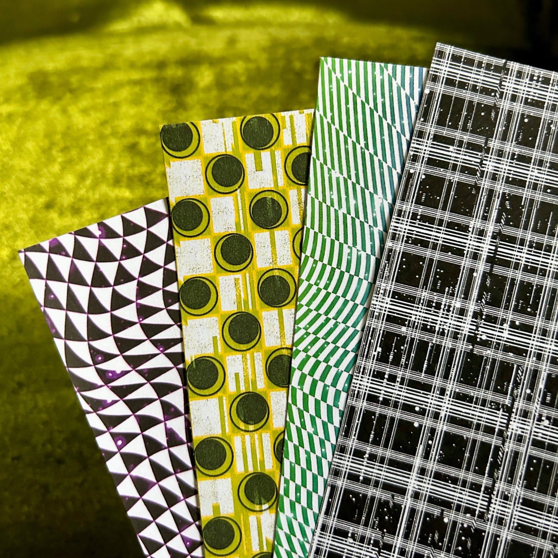 Four sheets of patterned sticker paper with geometric and plaid designs on a green background.