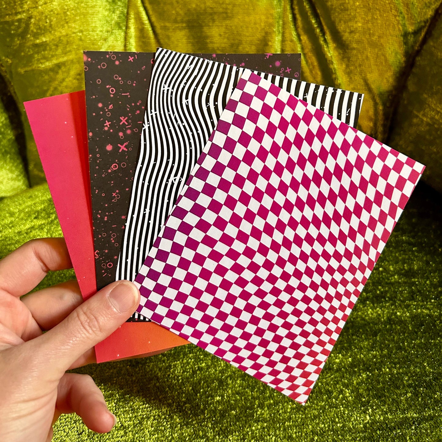 Hand holding four patterned paper sheets against a green fabric background