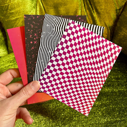 Hand holding four patterned paper sheets against a green fabric background