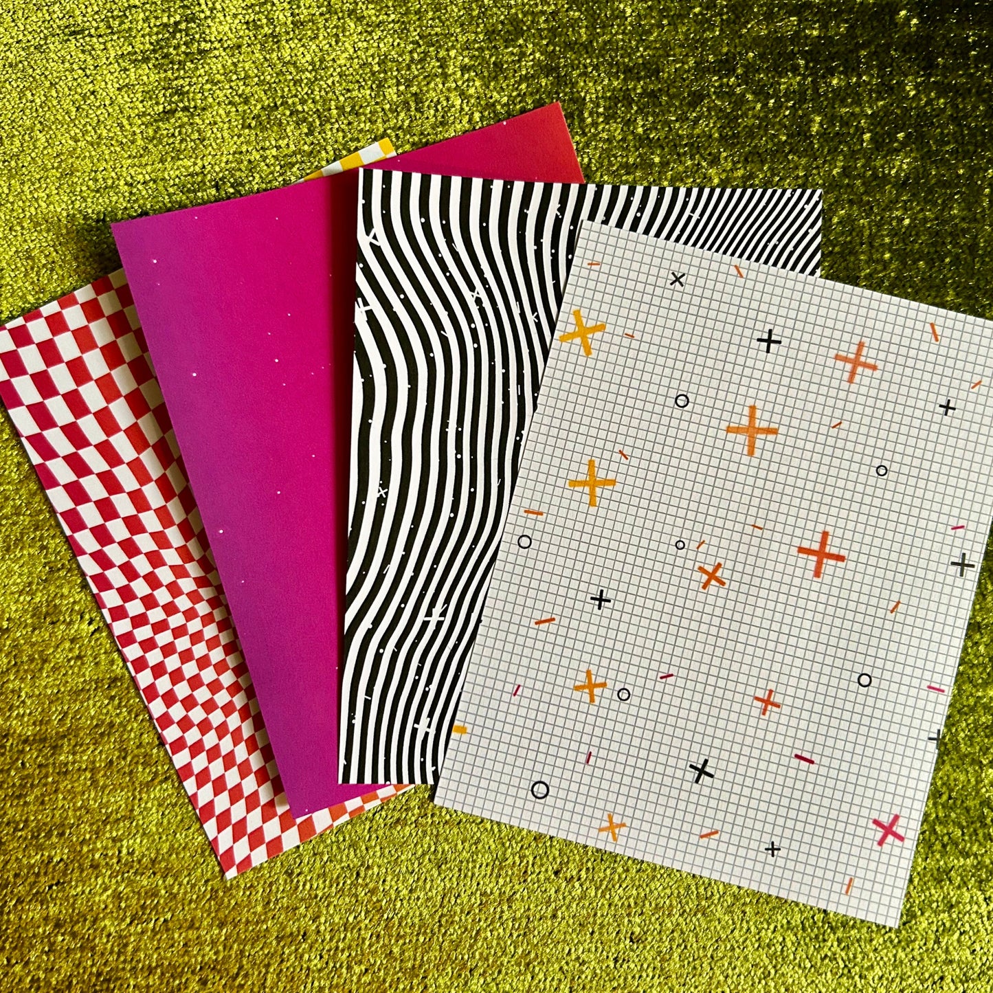 Four patterned pieces of sticker paper on a textured green surface