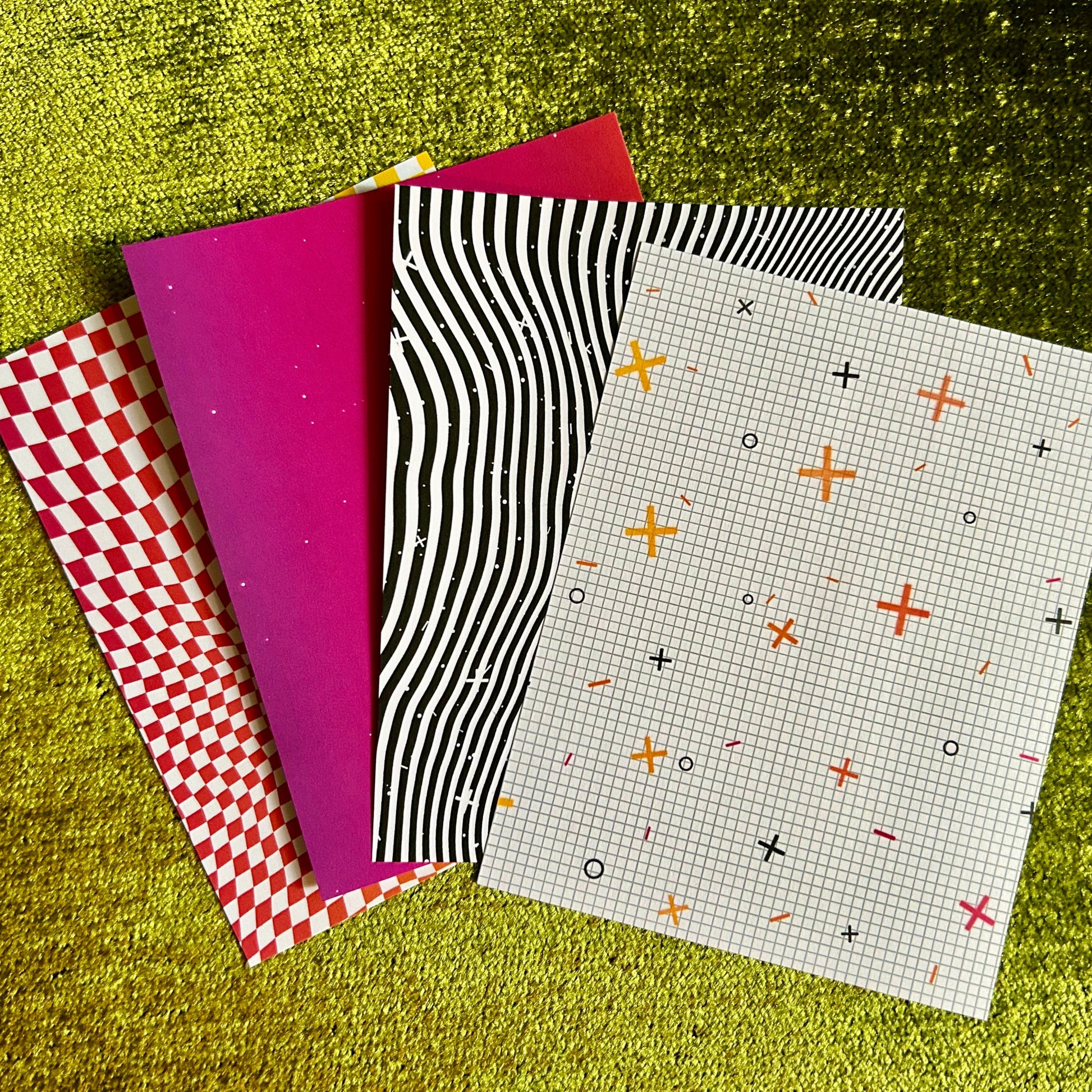 Four patterned pieces of sticker paper on a textured green surface