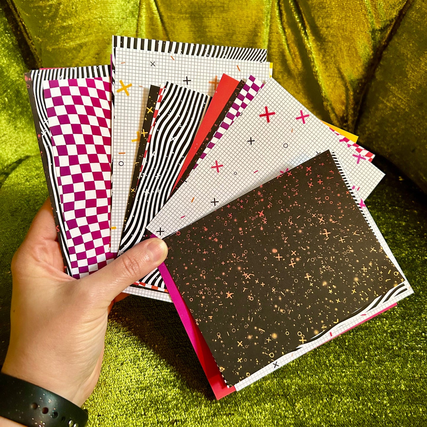 Hand holding a stack of patterned pieces of paper on a green textured surface