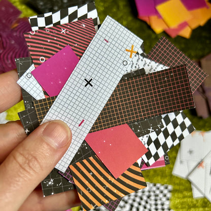 Hand holding a small ruler with patterned paper pieces on a textured surface