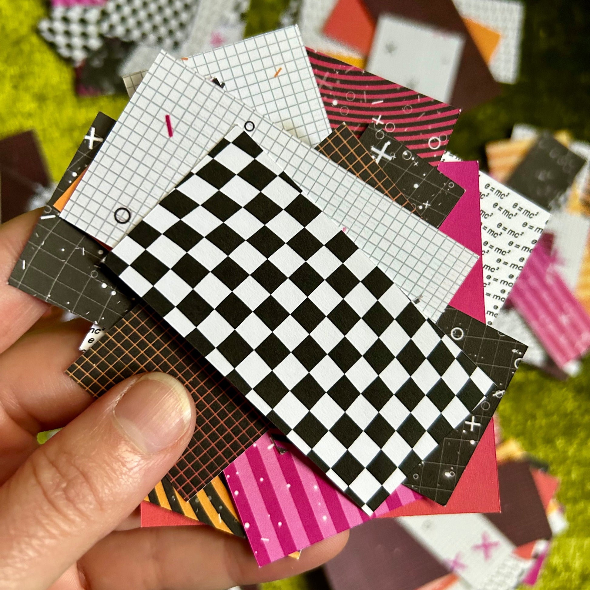 Hand holding a collection of small paper squares with various patterns on a grassy background