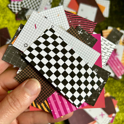 Hand holding a collection of small paper squares with various patterns on a grassy background