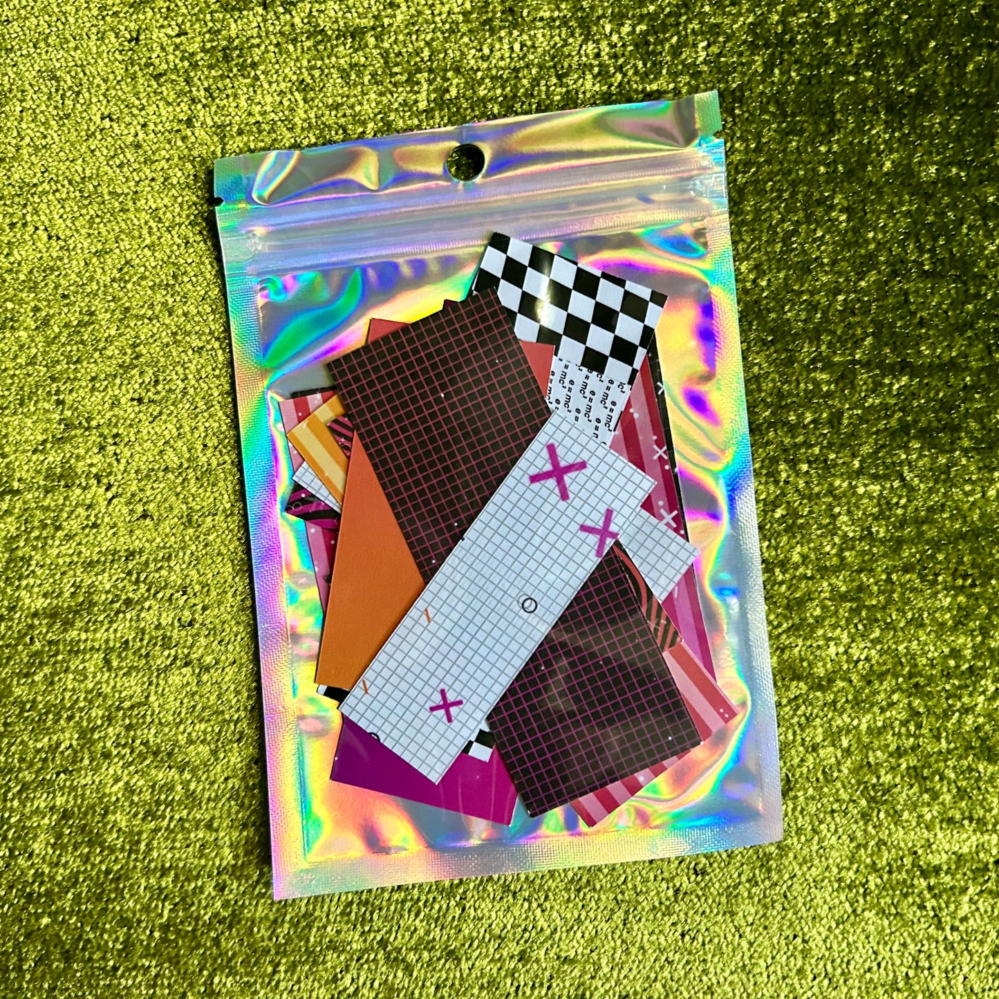 Holographic pouch with colorful sticker scraps on a green textured background