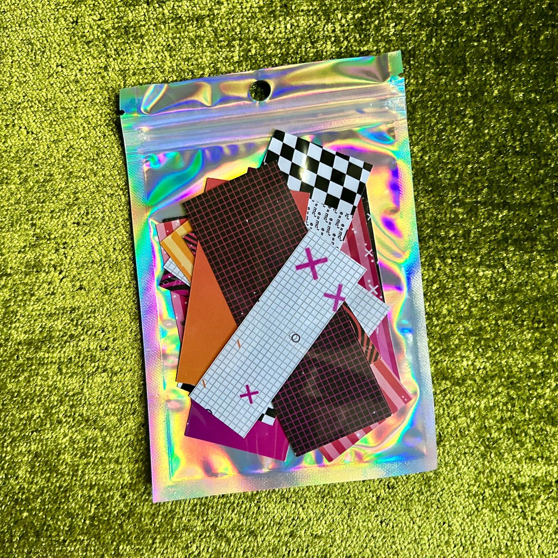 Holographic pouch with colorful sticker scraps on a green textured background