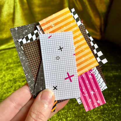 Hand holding a stack of small patterned sticker scraps against a green fabric background
