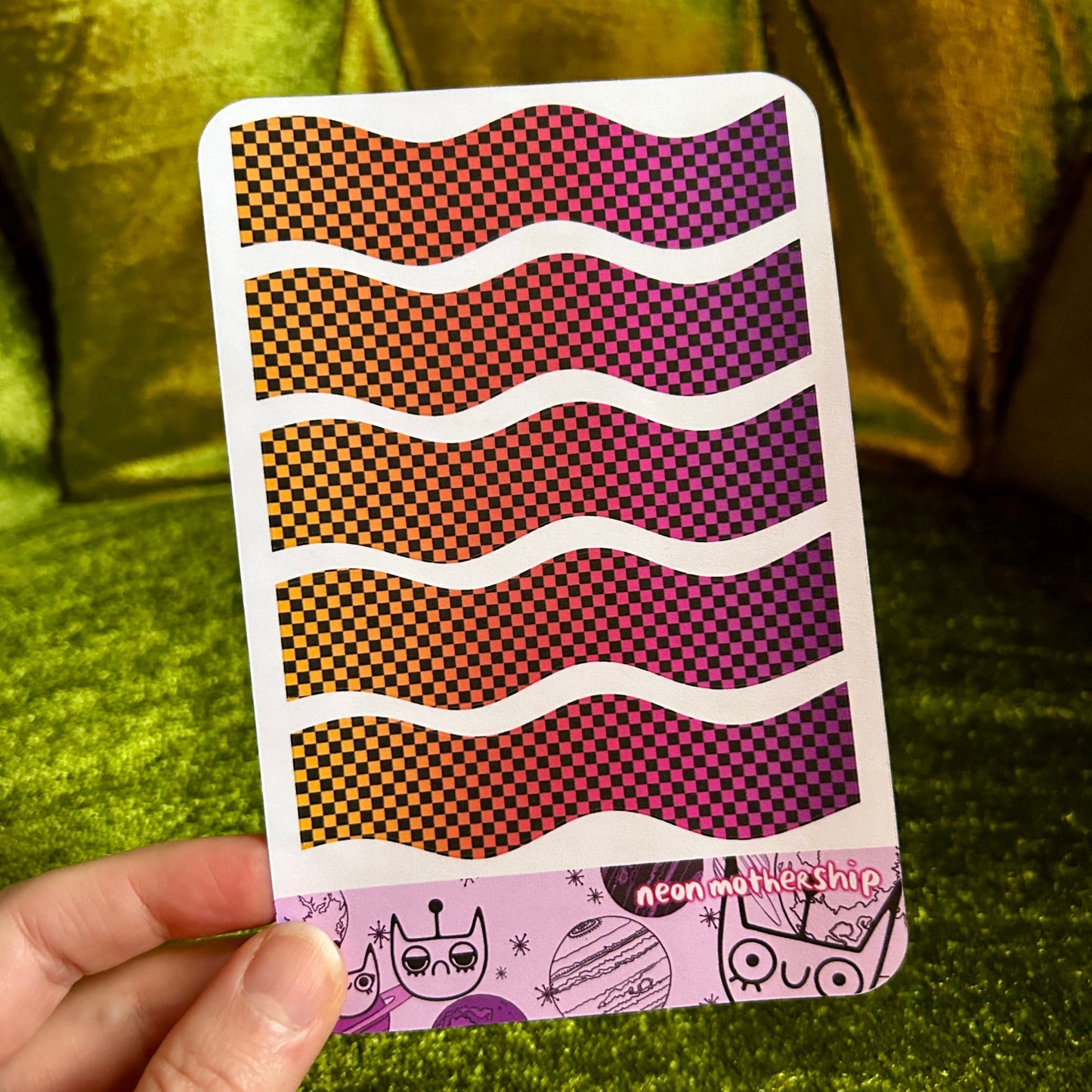 sticker sheet with wavy pattern held by a hand against a green textured background