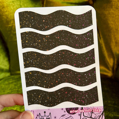 sticker sheet with wavy patterns and cartoon designs held by a hand on a green background