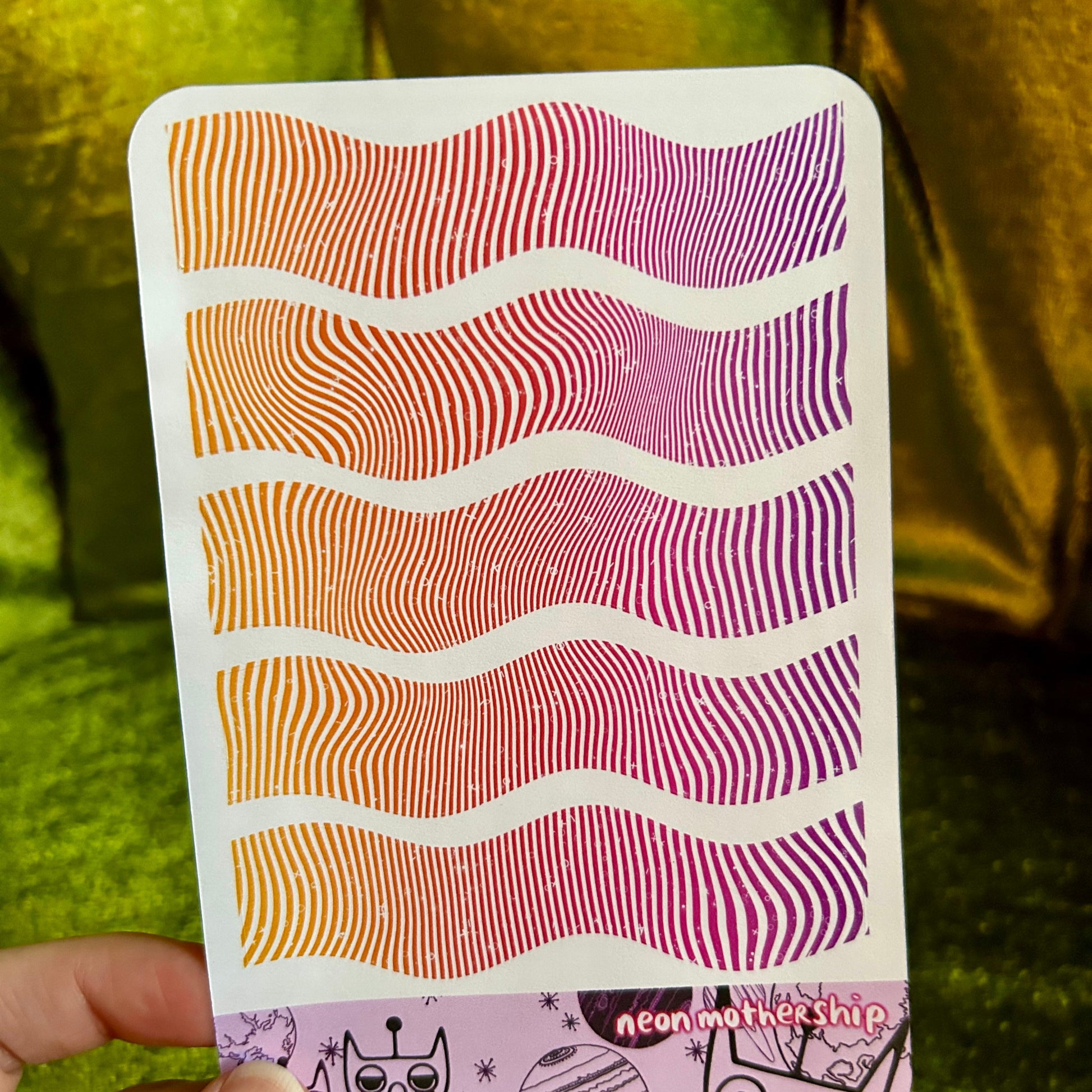 sticker sheet with wavy pattern held by a hand against a green fabric background