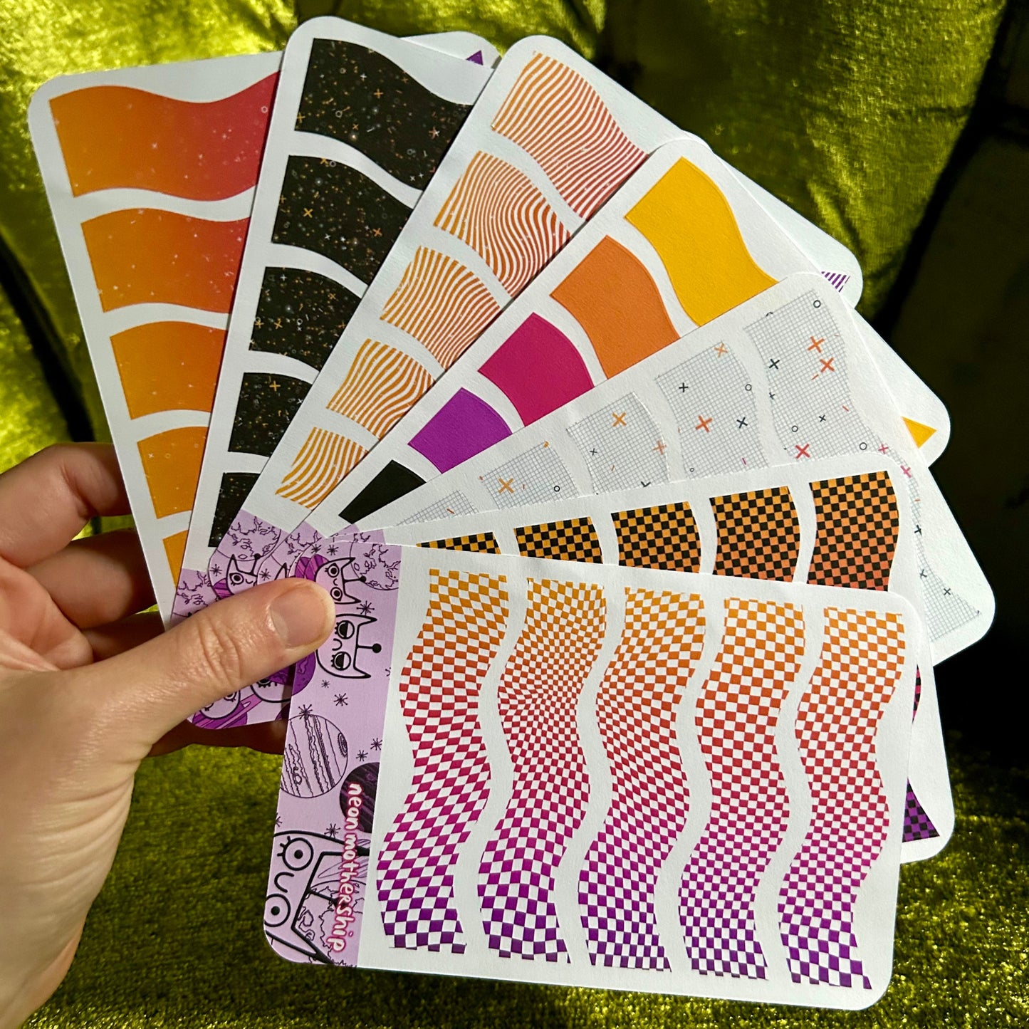 Hand holding a set of colorful sticker sheets against a green textured background