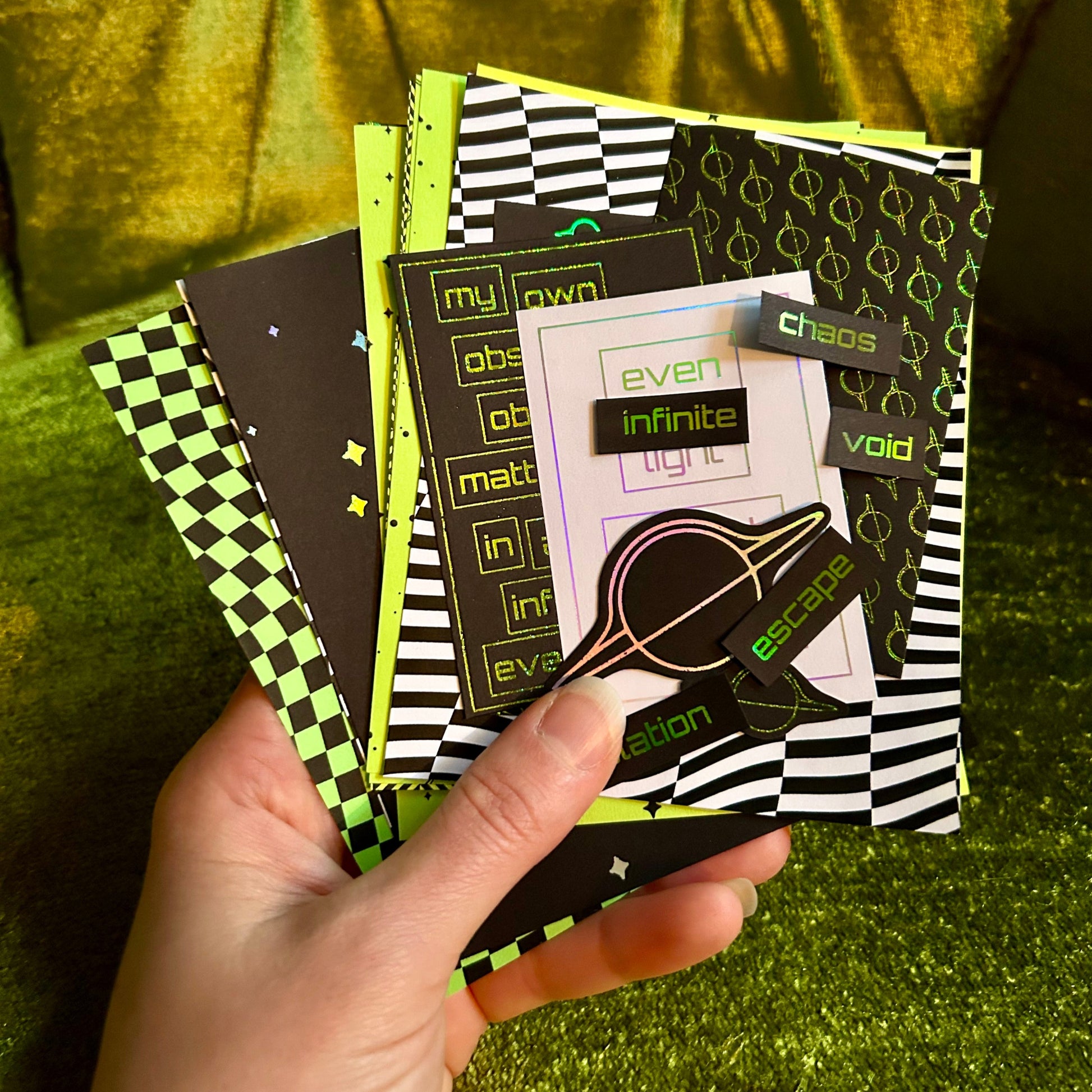 Hand holding a stack of patterned papers against a green fabric background