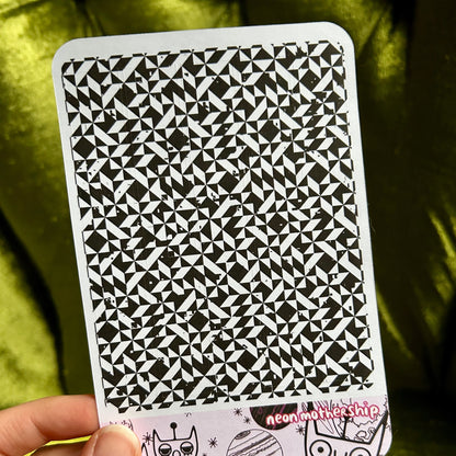sticker sheet with black and white pattern held by a hand against a green background