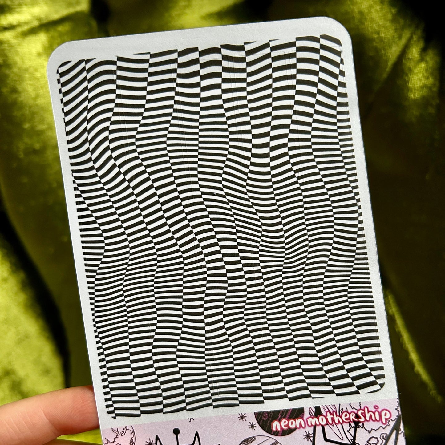 sticker sheet with black and white wavy pattern held by a hand against a green fabric background
