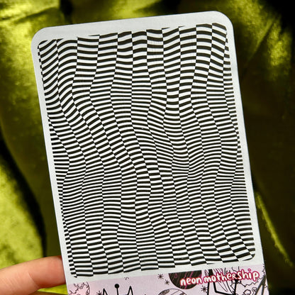 sticker sheet with black and white wavy pattern held by a hand against a green fabric background