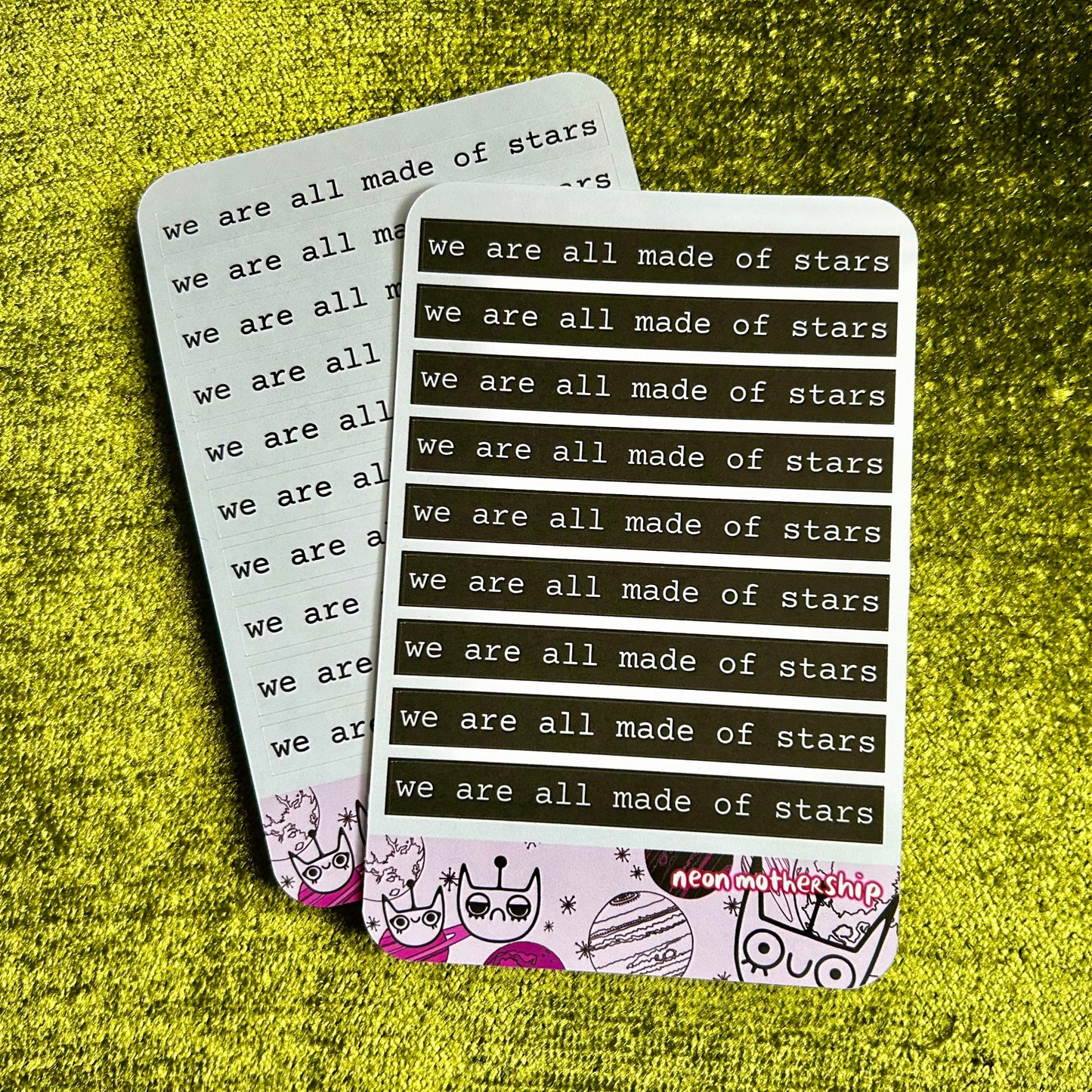 Two sticker sheets with 'we are all made of stars' text on a textured green surface