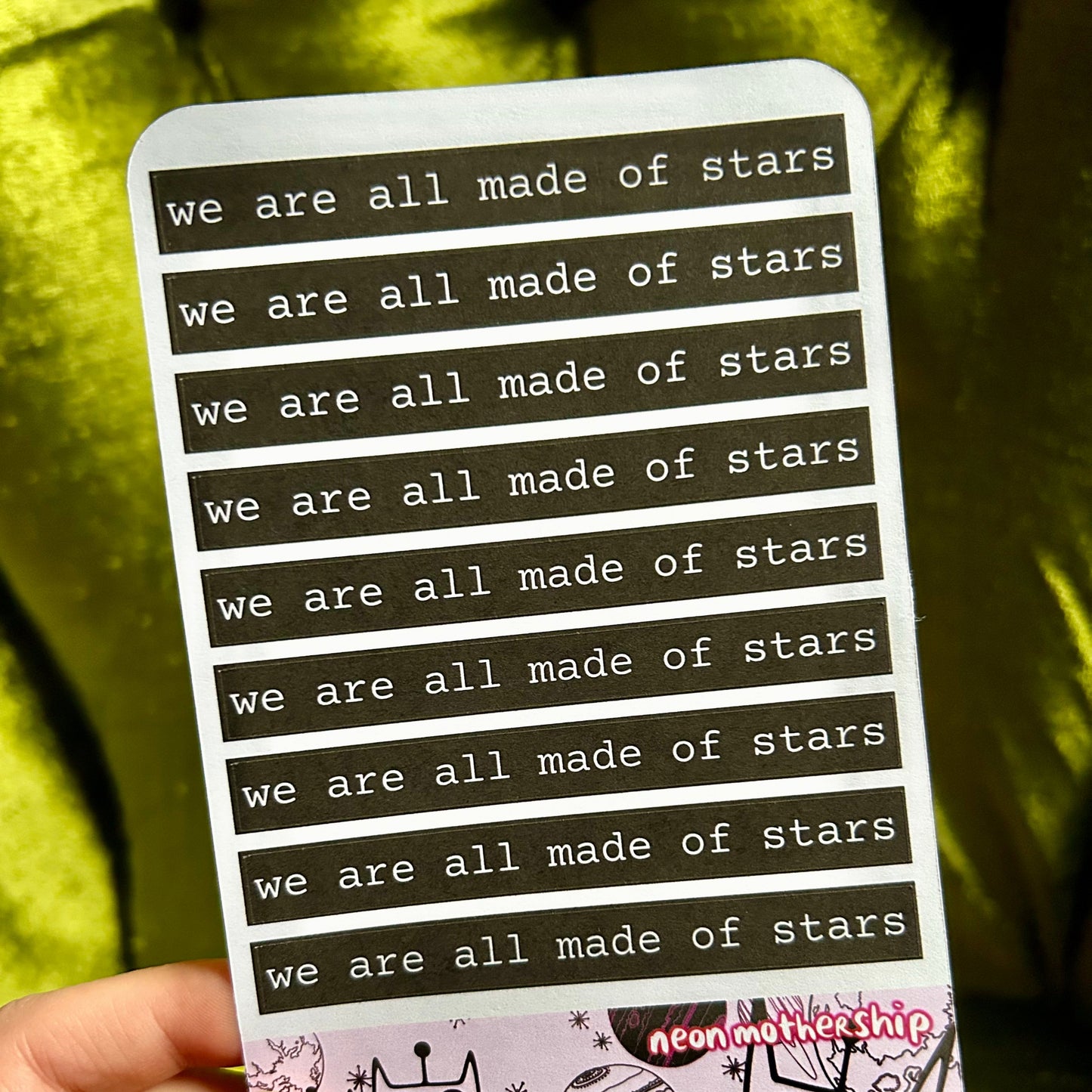 sticker sheet with 'we are all made of stars' text held by a hand against a yellow background